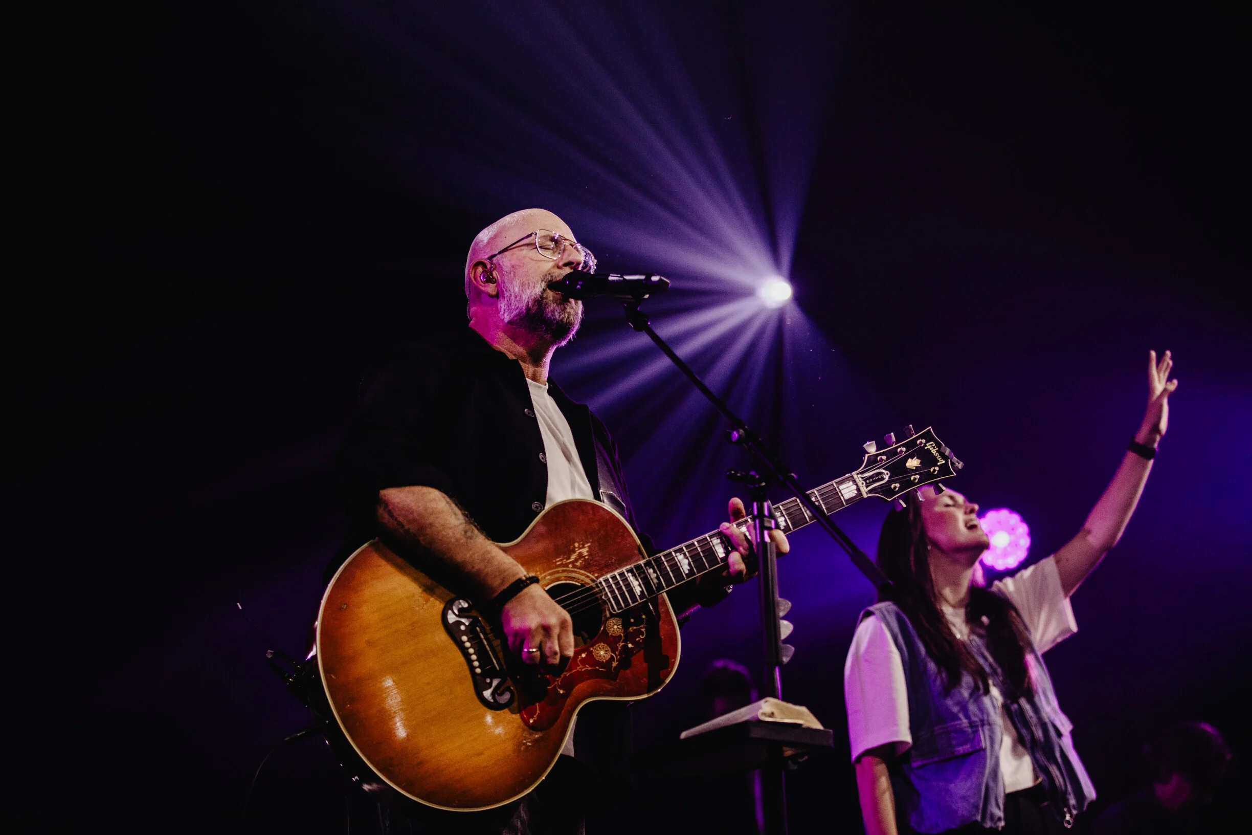 Kees Kraayenoord met akoestische gitaar en een zangeres van Mozaiek Worship op het podium