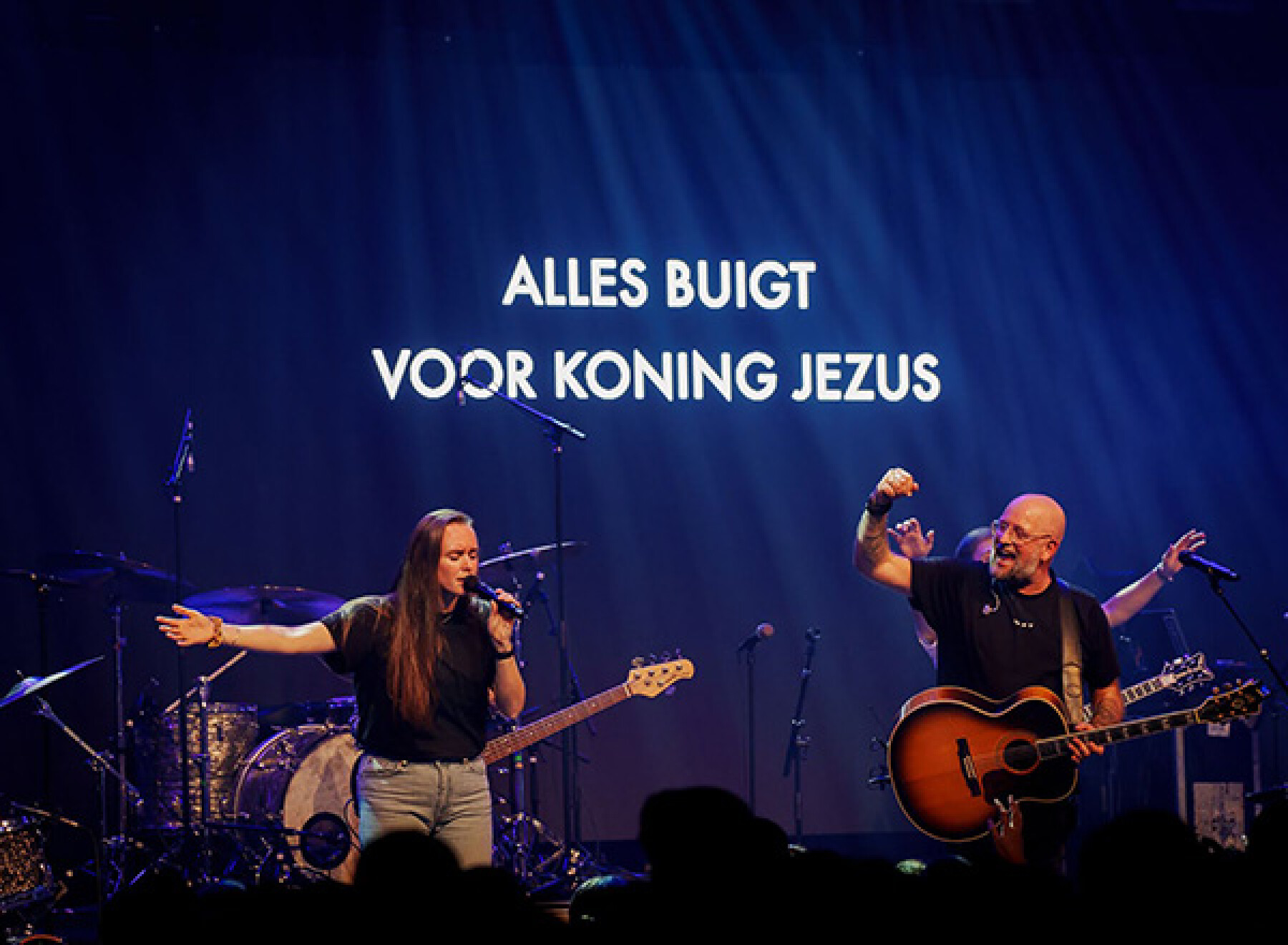 Mozaiek Worship op het podium met op het scherm de tekst Alles buigt voor Koning Jezus