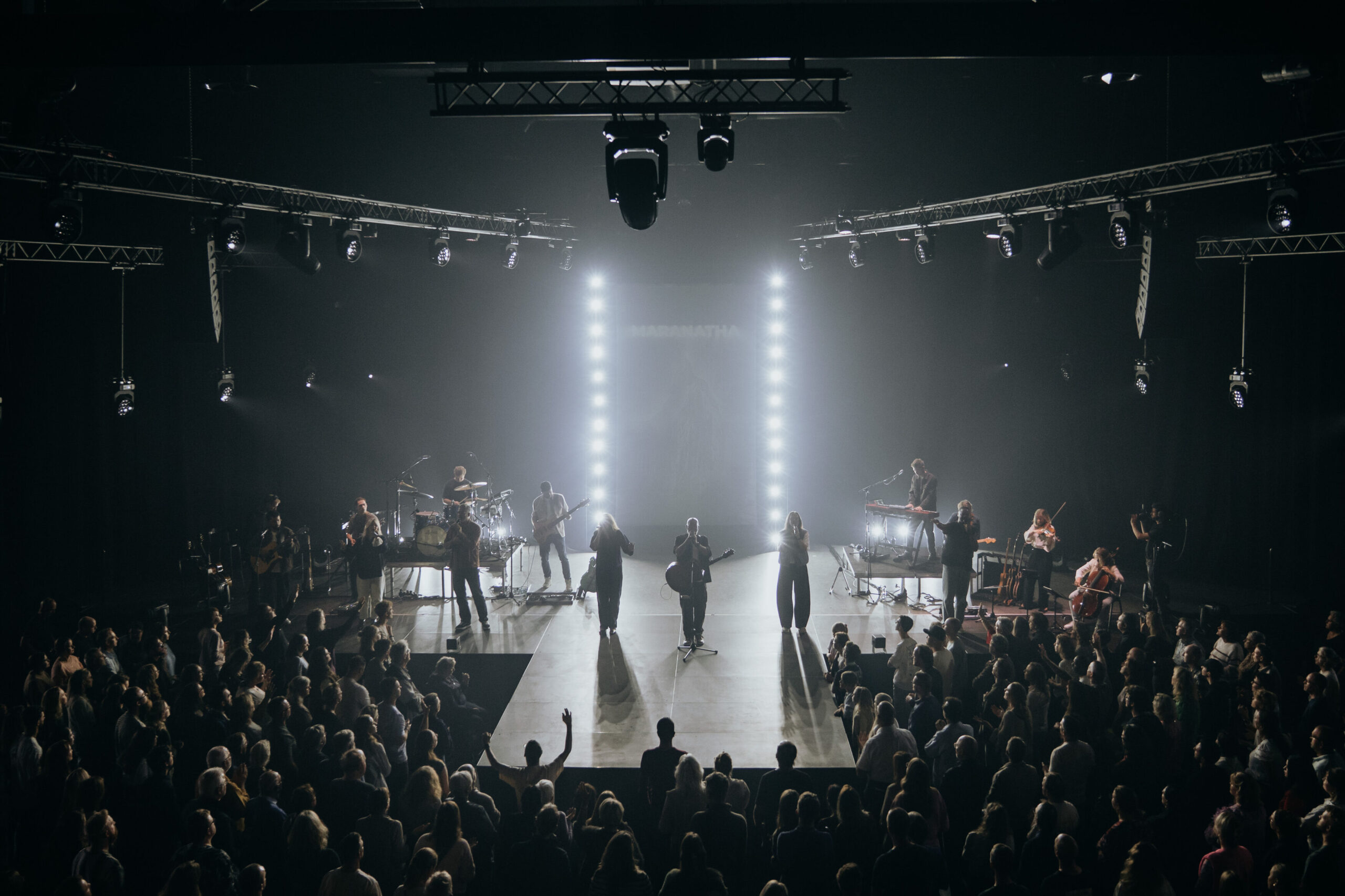 Mozaiek Worship op het podium tussen twee verticale lichtbalken tijdens de live-opname