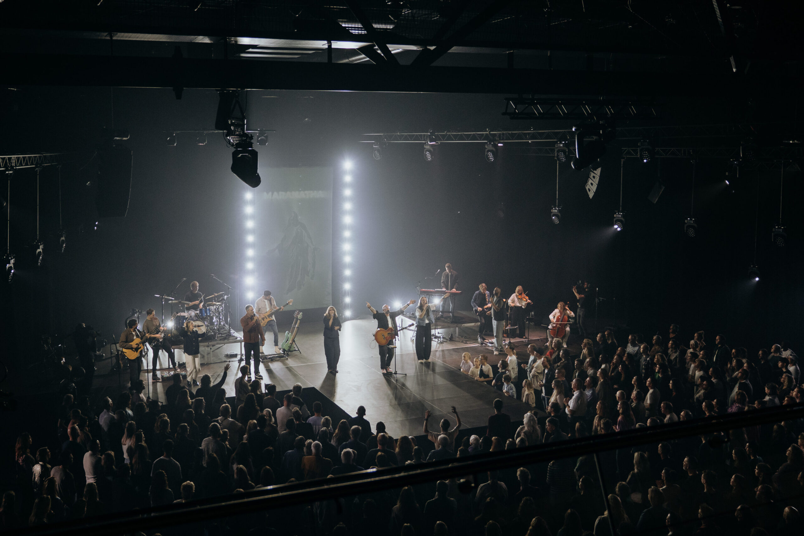 De band van Mozaiek Worship breed opgesteld op het podium in wit podiumlicht